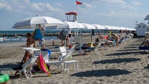 A beach with rows of white umbrellas and lounge chairs, a lifeguard tower, and a clear sky.