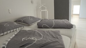 A bedroom with a bed, pillows, a hanging light, and a door leading to another room. - Idyllisches Ferienhaus in Ostseenähe (Dorf Mecklenburg OT Rambow)