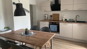 A modern kitchen with white cabinets, a black range hood, and a wooden dining table with chairs. - Idyllisches Ferienhaus in Ostseenähe (Dorf Mecklenburg OT Rambow)