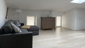 A modern loft bedroom with skylights, a grey sofa, a wooden dresser, and a wardrobe. - Idyllisches Ferienhaus in Ostseenähe (Dorf Mecklenburg OT Rambow)