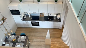 A modern kitchen with white cabinets, a black countertop, and a built-in oven. There are three potted plants on the countertop, and a dining area with a table set for four.