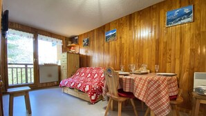 A cozy room with a bed, a dining table set for two, and a view of the outdoors through a window. - Cozy apt for 6, Praz-sur-Arly, free shuttle, parking, pets allowed (Praz-sur-Arly)