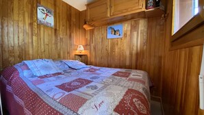 A wooden-paneled room with a bed, a wall-mounted lamp, and two framed pictures. - Cozy apt for 6, Praz-sur-Arly, free shuttle, parking, pets allowed (Praz-sur-Arly)