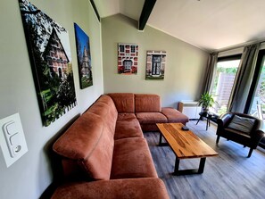 Un salon moderne avec un canapé d’angle, une table basse en bois et une grande fenêtre agrémentée de rideaux.