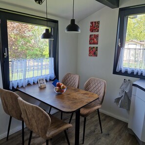 Un coin repas avec une table en bois, des chaises rembourrées, un saladier de fruits et une suspension.