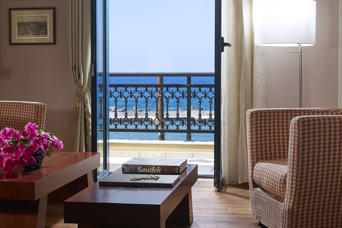 A room with a view of the sea, a table with a book, and two chairs.