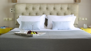 Habitación de hotel con cabecera capitonada, ropa de cama blanca, una bandeja con frutas y almohada a cuadros.