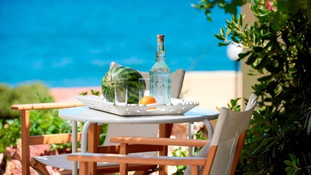 Una mesa con sandía, una botella y vasos sobre una bandeja, dispuesta al aire libre con vista al mar.