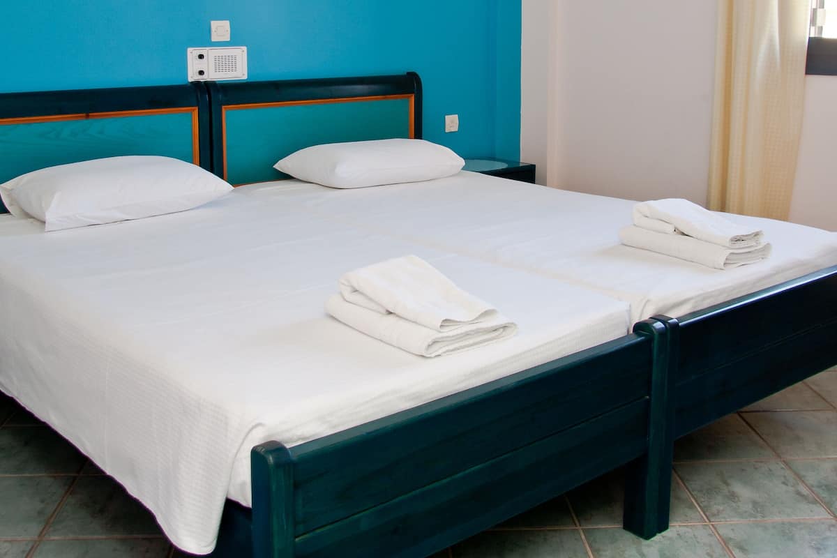 A neatly made bed with white linens and towels, a blue wall, and a tiled floor.