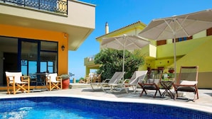 Una piscina con sillas de descanso y sombrillas, rodeada de edificios con balcones y grandes ventanales.