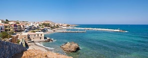 A coastal town with buildings along the shore, a rocky outcrop, and a clear blue sea. - Marelina Villas (Mylopotamos)