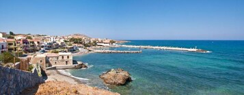 Μια παραθαλάσσια πόλη με κτίρια που εκτείνονται κατά μήκος της ακτής, ένα βραχώδες ακρωτήρι και μια καθαρή, γαλάζια θάλασσα.