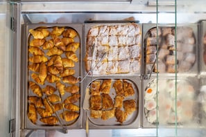 A bakery display with various baked goods including croissants, puff pastries, and a dusting of powdered sugar on a cake. - Marelina Villas (Mylopotamos)