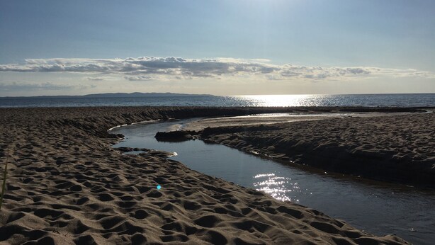 En strand med en bæk, under en klar himmel.