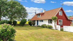 Et rødt og hvidt hus med et tegltag, omgivet af en velplejet græsplæne og træer.