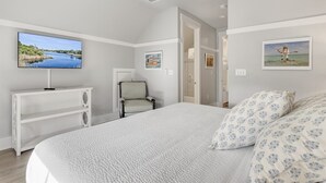 A bedroom with a bed, a TV mounted on the wall, a chair, and artwork. - Watercolor Resort|Close To Pool | 6 Pass Golf Cart (Santa Rosa Beach)