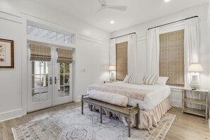 Um quarto com cama, mesas de cabeceira, um banquinho, um tapete e um ventilador de teto.