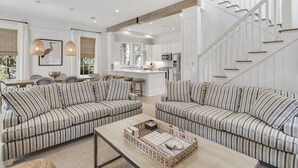 A spacious living area with striped sofas, a coffee table, and a kitchen in the background. - Watercolor Resort|Close To Pool | 6 Pass Golf Cart (Santa Rosa Beach)