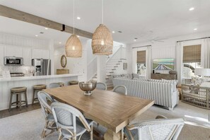 Een moderne keuken met witte kastjes, een houten eettafel, rieten stoelen en hanglampen.
