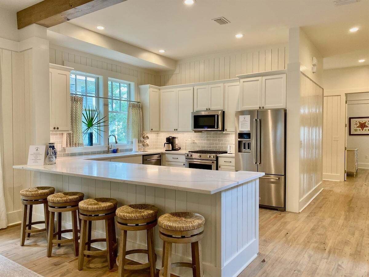 A kitchen with a central island, bar stools, stainless steel appliances, and a large window.