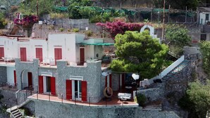 Un immeuble à plusieurs étages, doté de volets rouges, d’une façade en pierre et d’un escalier menant à un balcon.