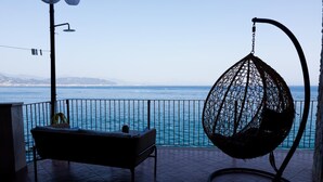 Un balcon doté d’un fauteuil suspendu en osier et d’un banc rembourré, offrant une vue sur la mer.