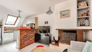 A compact kitchen with a brick accent wall, a dining area with a red chair, and a living space with a sofa and fireplace. - 300m beach, lovely house, 6 adults 1 child (Sarzeau)