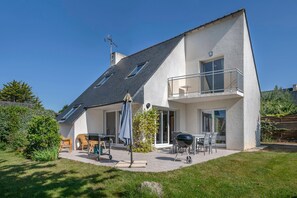 Et toetagers hus med balkon, terrasse med udendørs møbler og grill.