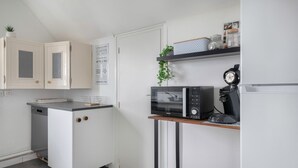 Kompakti keittiö, jossa on valkoiset kaapit, mikroaaltouuni, kahvinkeitin ja pieni astianpesukone.