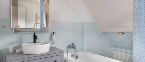 A bathroom with a white sink, mirror, and bathtub.