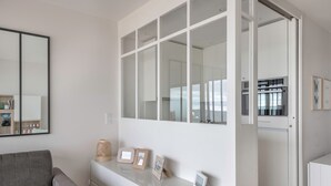 Uma sala de estar moderna com um sofá cinzento, uma mesa consola branca com fotografias emolduradas e um espelho grande na parede.