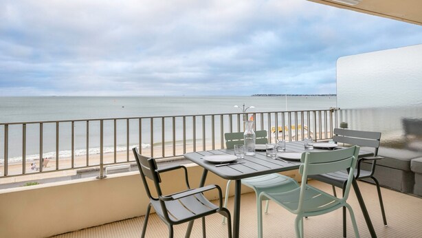 Varanda com mesa e cadeiras, com vista para a praia e o mar.