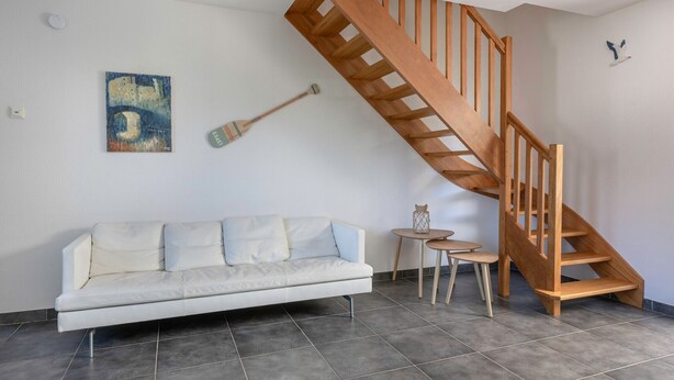 Un salon moderne avec un canapé blanc, un escalier en bois, une petite table et un tableau accroché au mur.