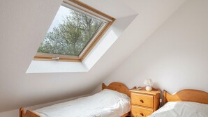 Une petite chambre avec un lit simple, une lucarne, des meubles en bois et une table de chevet.