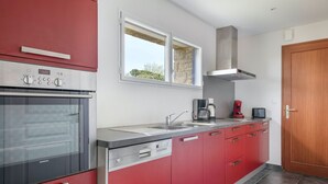 Une cuisine moderne avec des meubles de couleur rouge, des appareils électroménagers en acier inoxydable, une fenêtre et une porte en bois.