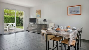 Un coin repas avec une table mise pour le petit-déjeuner, un téléviseur posé sur un meuble et une vue sur la verdure à travers la porte-fenêtre coulissante.