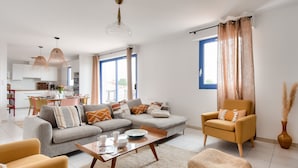 Una sala de estar moderna con un sofá, un sillón y una mesa de centro. Se ve un área de comedor con una mesa y sillas al fondo.