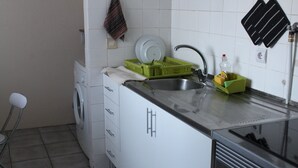 Pieni, käytännöllinen keittiö, jossa on pyykinpesukone, pesuallas ja astiateline.