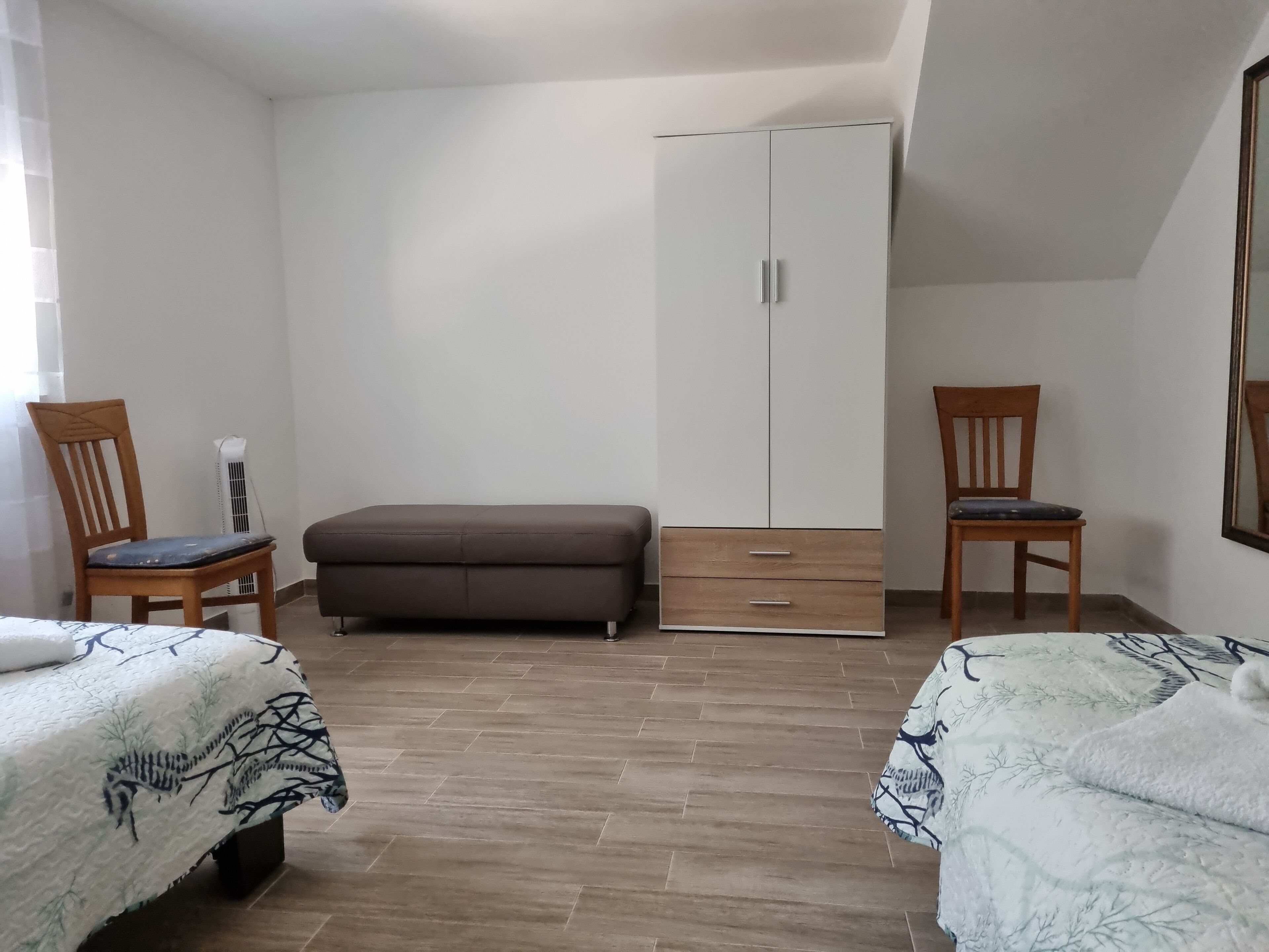 Een slaapkamer met twee bedden, een kast en twee houten stoelen.