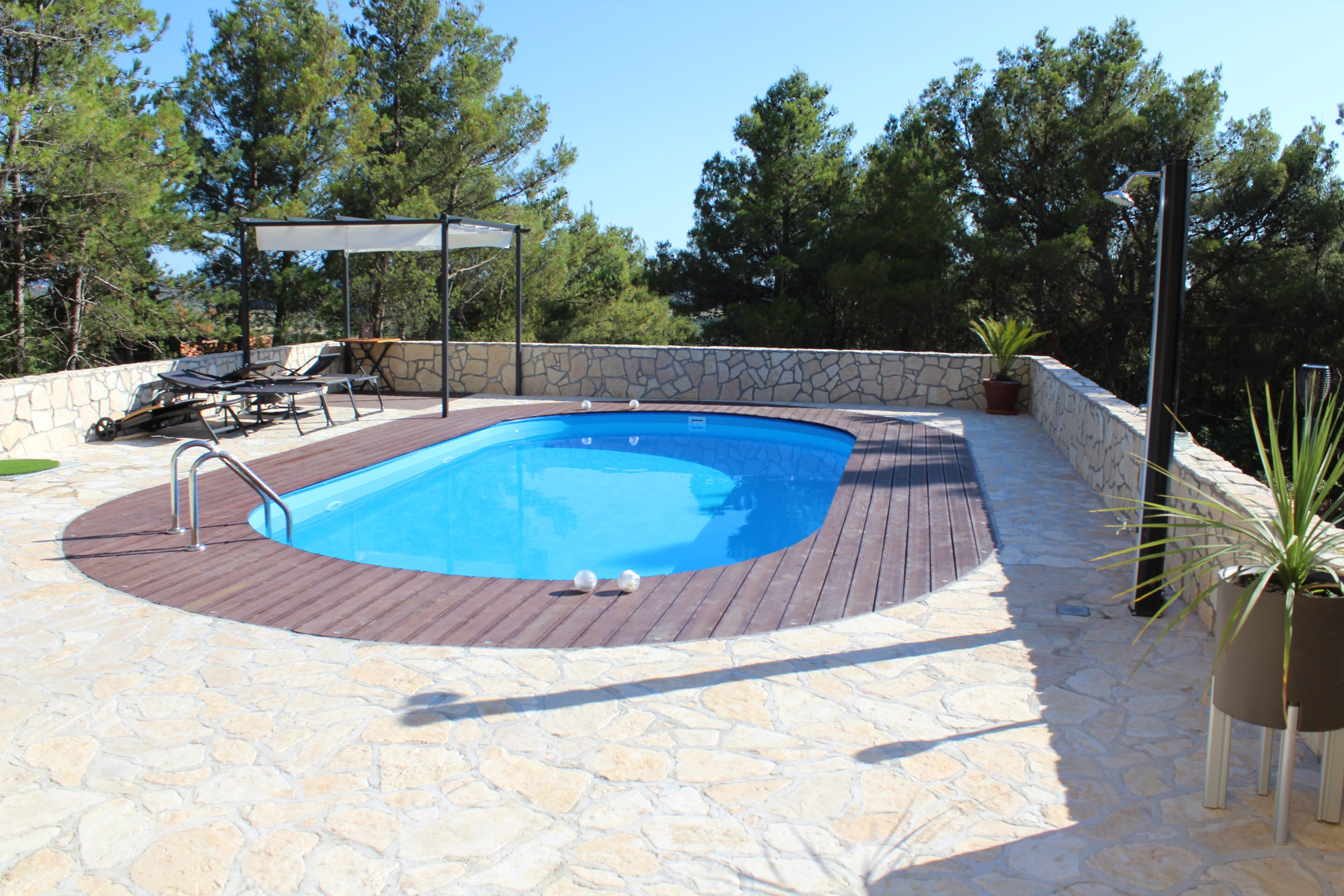 Ein Pool mit einer Steindeck, umgeben von Liegestühlen und einer Pergola.