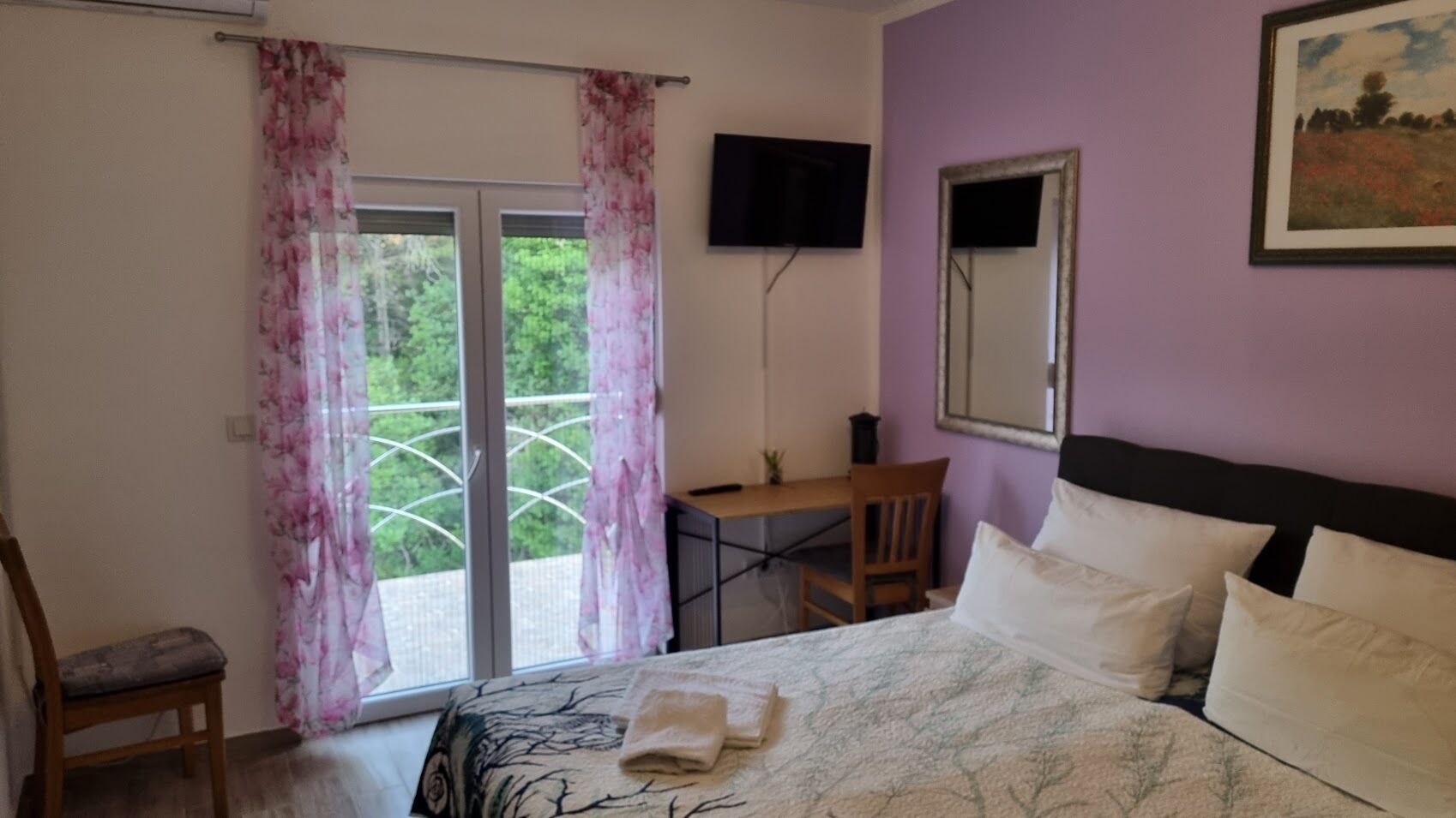 Un dormitorio con cama, escritorio, silla, televisor y ventana con cortinas.