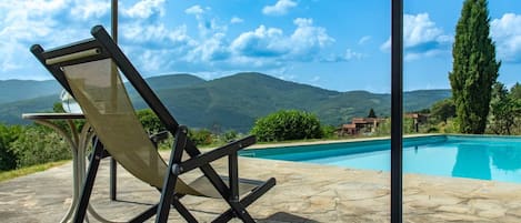A poolside area with a chair and a table, overlooking a mountain landscape.