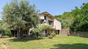 A two-story house with a stone wall, a large tree, and a well-maintained lawn.