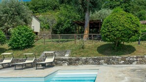A swimming pool with lounge chairs, a stone wall, and a rustic building surrounded by trees.