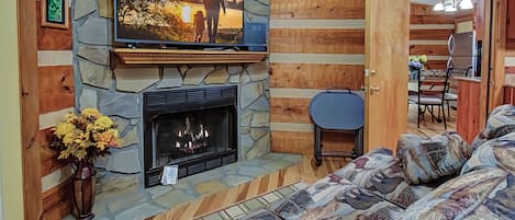 Un salon chaleureux avec une cheminée en pierre, un téléviseur fixé au-dessus et un canapé confortable.