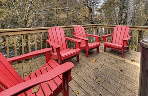 Une terrasse en bois avec des fauteuils Adirondack rouges et une rambarde en métal.