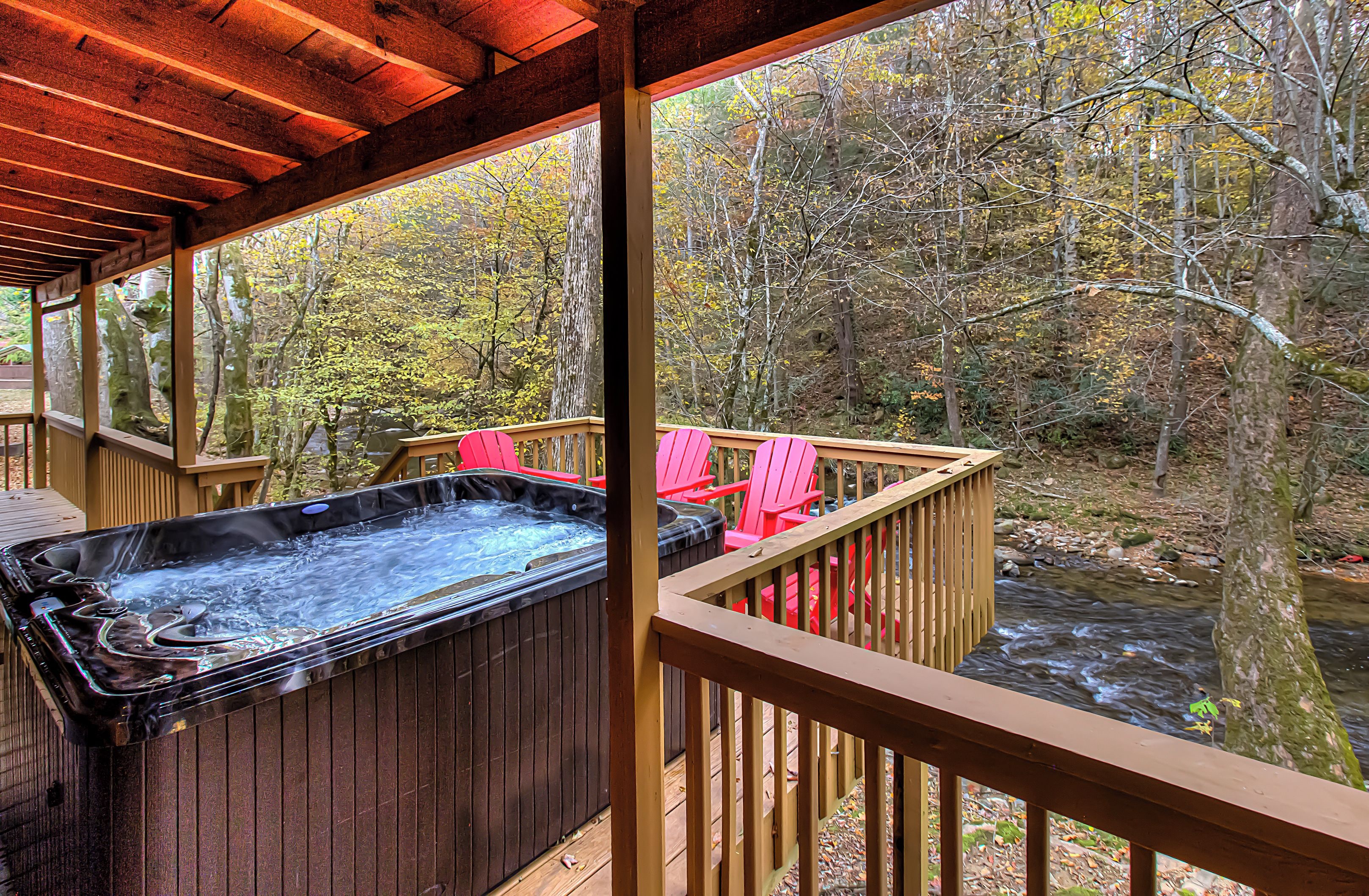 A hot tub on a wooden deck with a view of a forest and a stream.