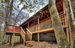 A wooden deck with a staircase leading to a covered area, surrounded by trees.