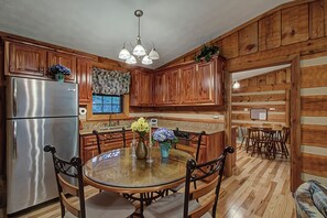 Cozinha com armários de madeira, geladeira de aço inoxidável, mesa de jantar de vidro com cadeiras e um lustre.