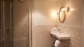 Un baño moderno con cabina de ducha de vidrio, un lavamanos blanco con espejo e iluminación en la pared.